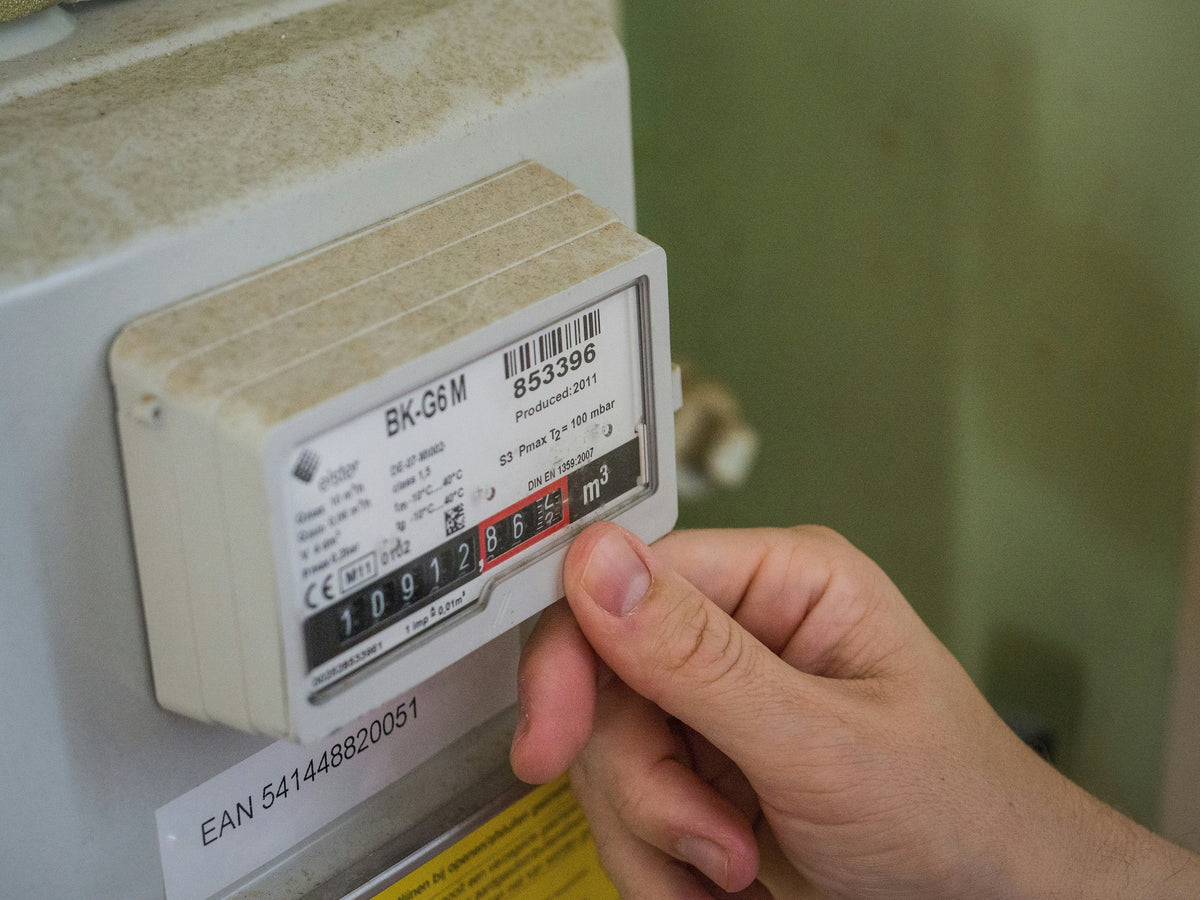 Una mano señalando la pantalla analógica de un contador de gas doméstico instalado en la pared, mostrando la lectura del consumo en metros cúbicos.