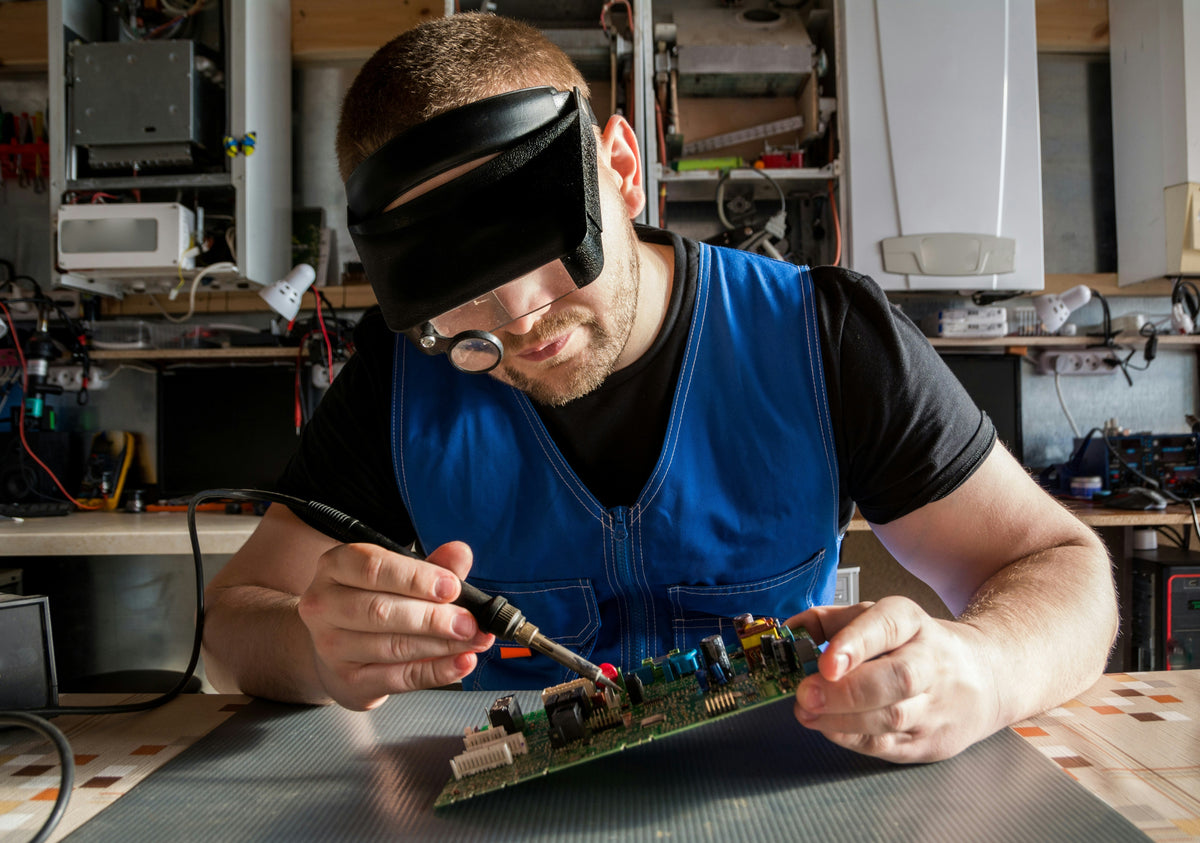 Un técnico con gafas de aumento soldando componentes electrónicos en una placa de circuito impreso en su taller.