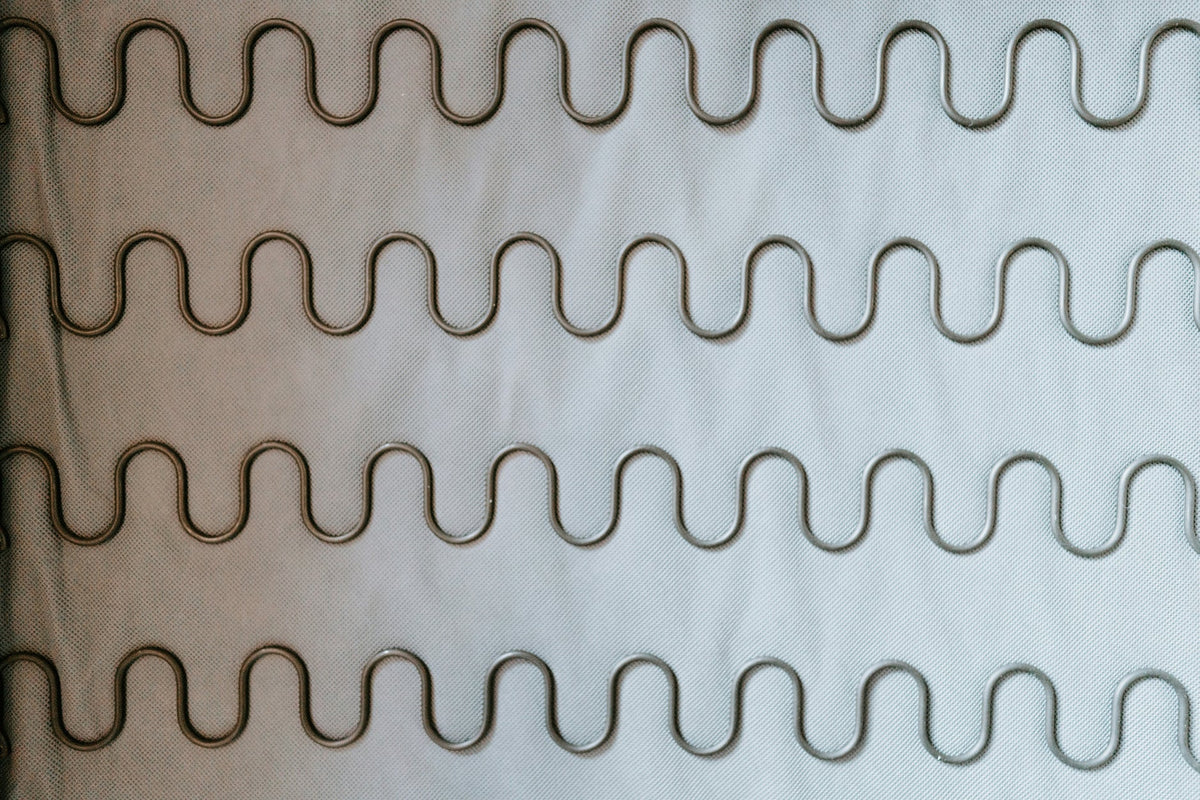 Primer plano de una estructura de muelles de acero en zigzag o sinusoidales sobre una base de tela gris para la fabricación de un sofá o sillón.
