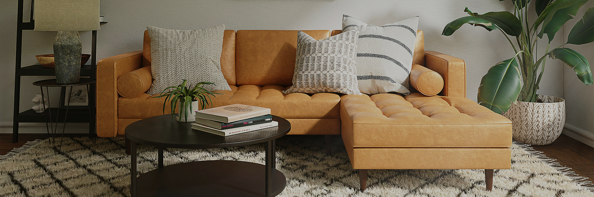 A modern mustard yellow sectional sofa with a tufted chaise lounge, styled with neutral throw pillows in a cozy living room setting with a black coffee table and a potted plant.