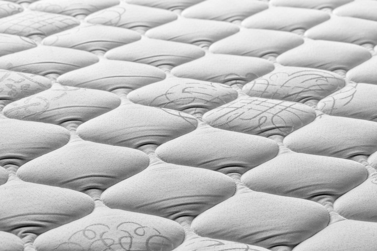 Primer plano de la superficie de un colchón blanco acolchado con patrón en relieve de rombos y detalles bordados.