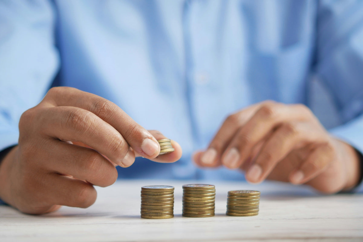 Primer plano de las manos de una persona con camisa azul apilando y contando monedas doradas sobre un escritorio de madera clara.