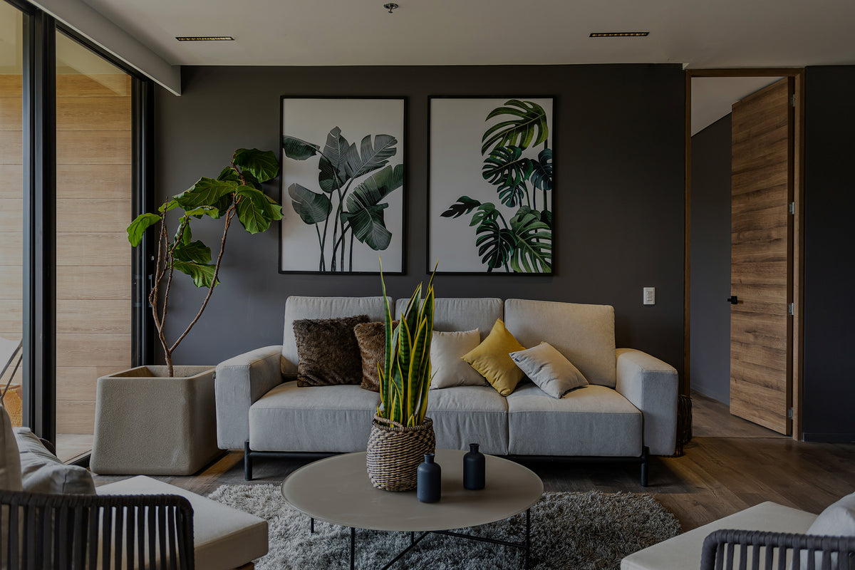 A modern living room featuring a light gray sofa with decorative pillows, a round coffee table, and two framed botanical prints on a dark gray wall.